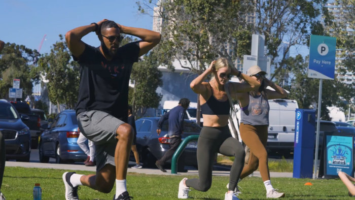 Three People Exercising Outdoors at A Fitness Event, with Cars and Urban Buildings in The Background