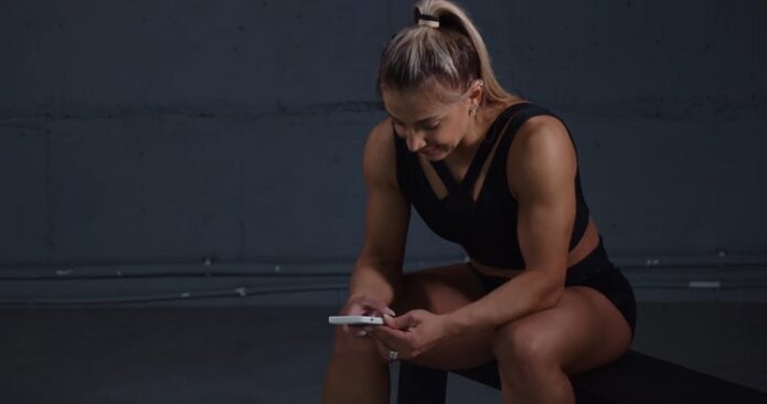 A muscular woman checks her phone to manage her publishing schedule for fitness clips