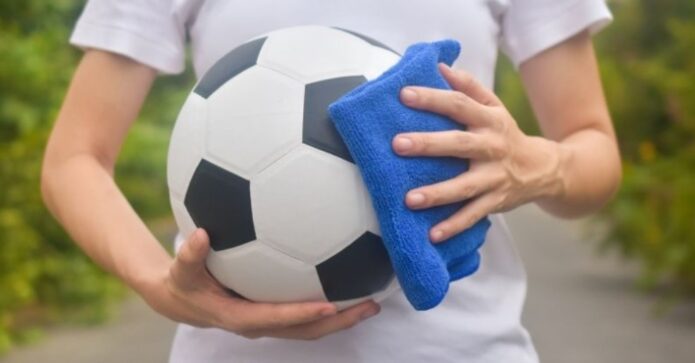 A person cleaning soccer ball with a blue cloth